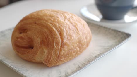 un croissant fresco y marrón dorado en un plato blanco con una taza de café