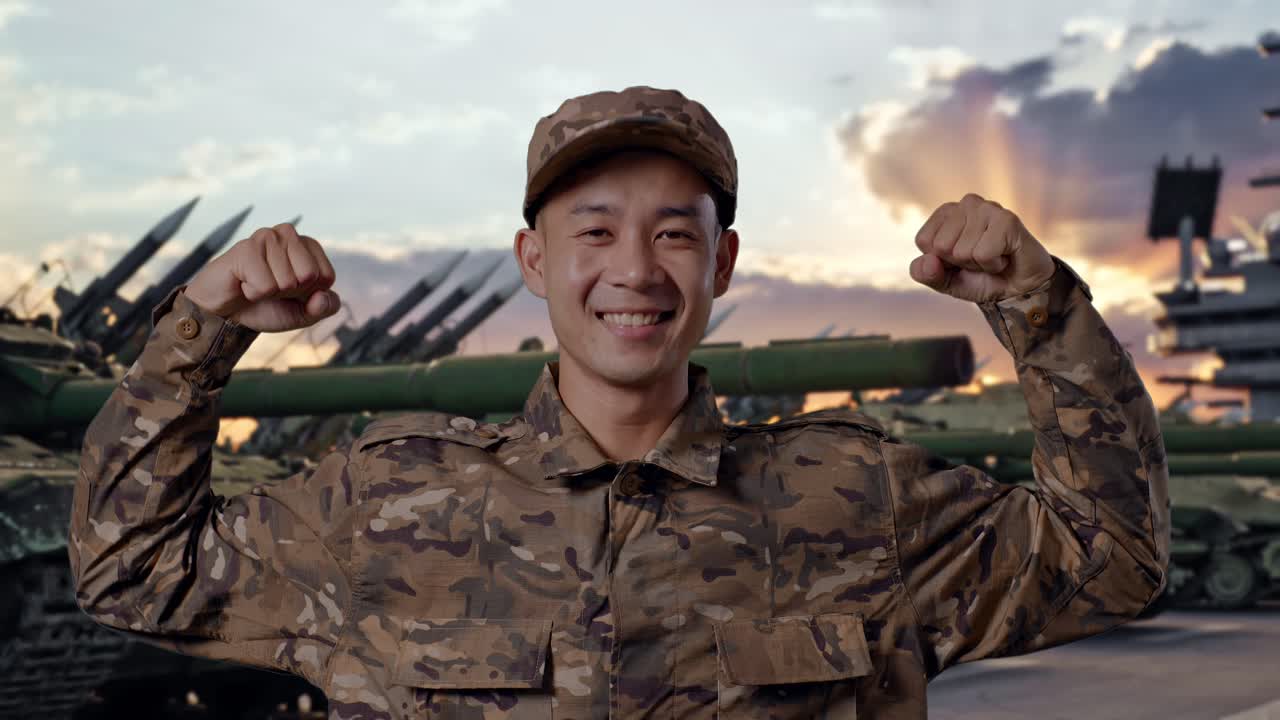 Primer plano de un soldado asiático sonriendo y flexionando el bíceps mientras está de pie junto a un tanque
