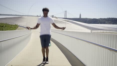 smiling african american sportsman skipping rope on bridge.