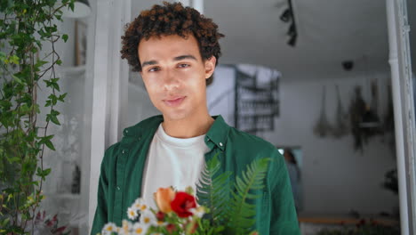 modelo romántico mira la cámara en la floristería. el hombre soñador disfruta del olor de las flores.