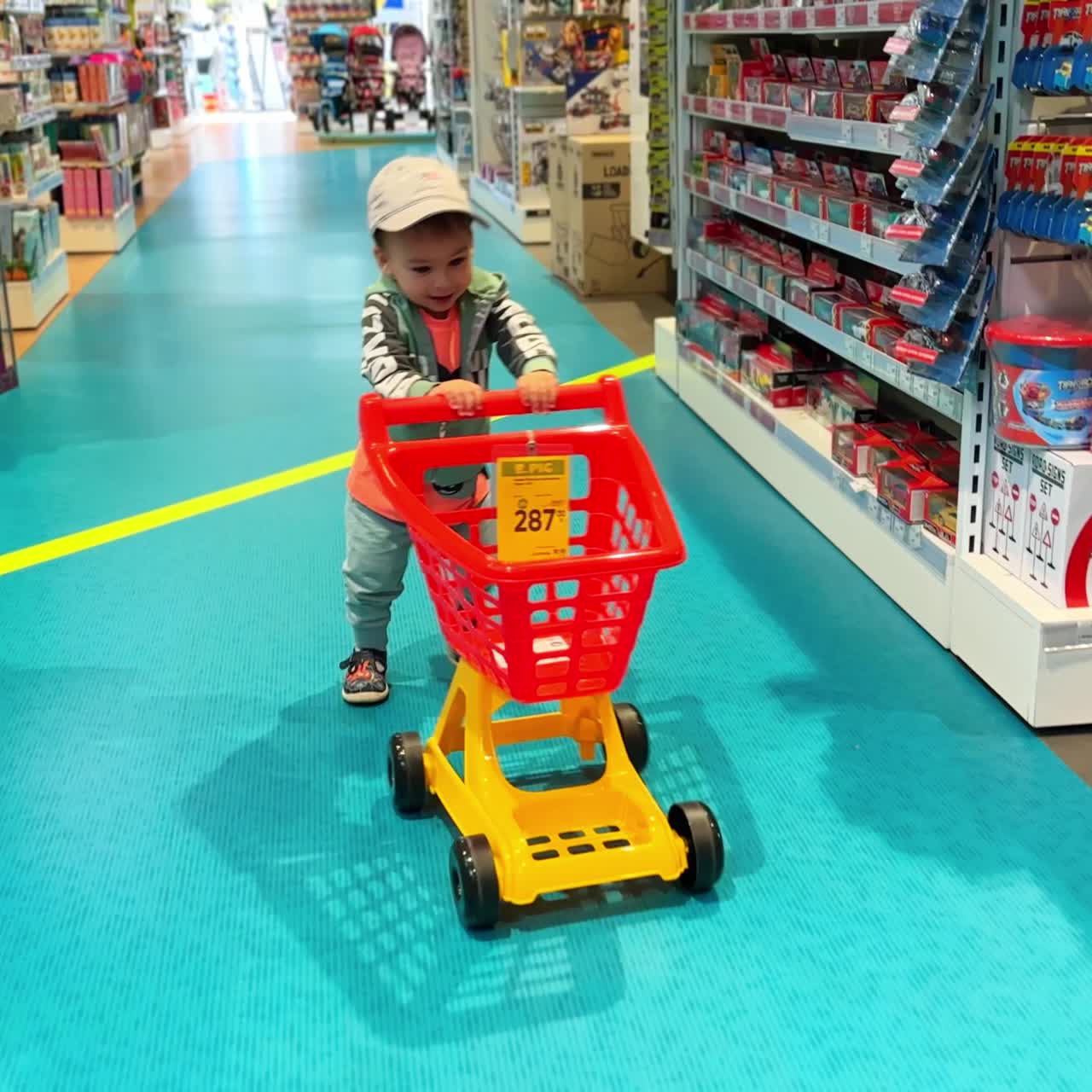 Excited baby boy pushing the red cart by the store isle. Cute child shopping in a toy shop