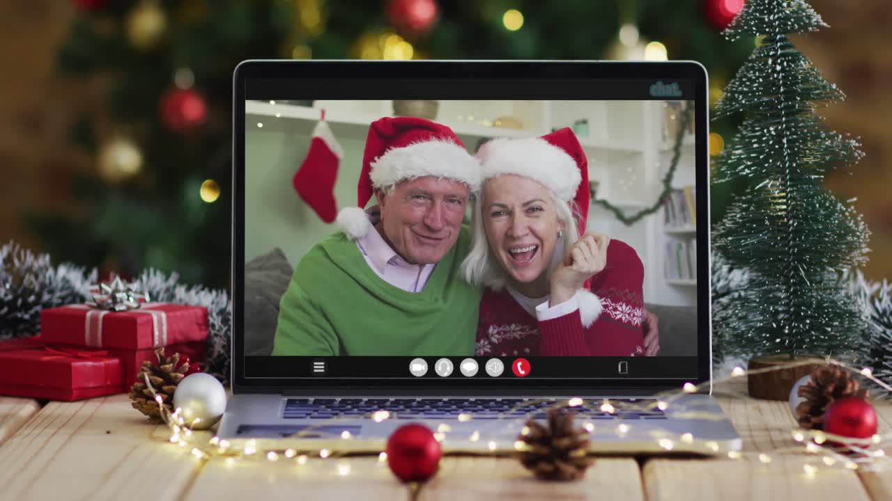 una pareja de alto nivel caucásica saludando en una videollamada en una computadora portátil, con un árbol de navidad