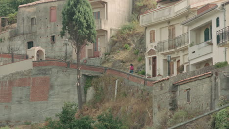 young woman walking up a path through a mountain village in italy, sunny savoca