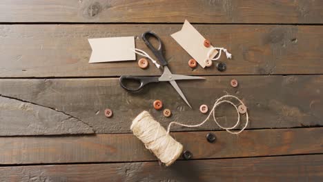 Video-of-scissors,-twine-string,-buttons-and-gift-tags-on-dark-wood-boards-with-copy-space