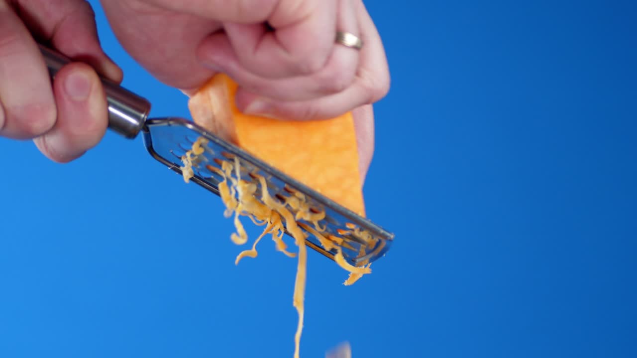 Male hand rubbed cheddar cheese on a grater.