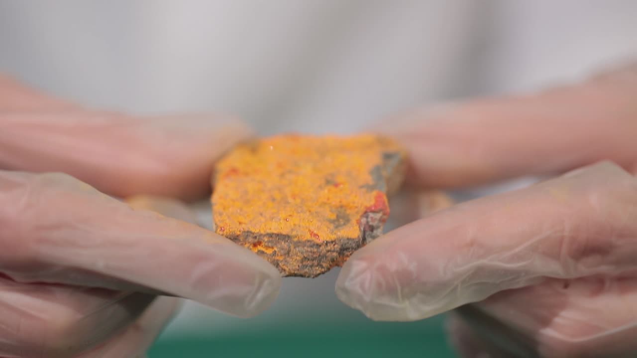 Scientist examining an orange mineral sample in a laboratory setting