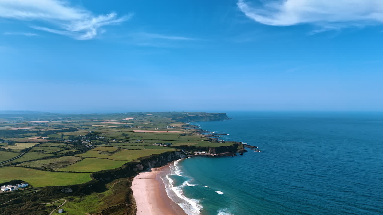 Stunning panorama of a rocky shore of Ireland with blue waterscape and sky. Aerial perspective on the scenery with farmlands and rare houses.