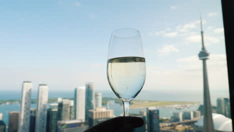 mano con una copa de vino contra el fondo de la ventana donde se encuentra la famosa torre cn de toronto