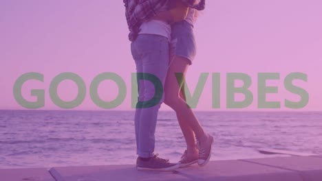 múltiples textos de buenas vibraciones contra la sección baja de una pareja caucásica abrazándose cerca del mar
