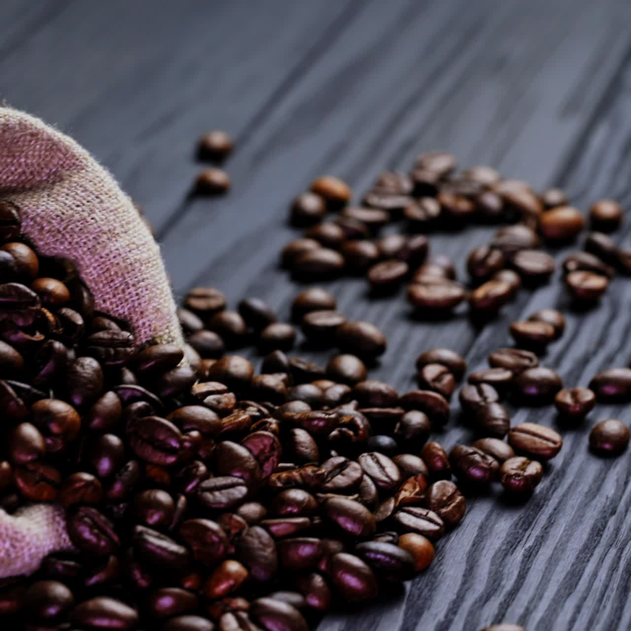 Scattered coffee beans on wooden background. Small sack on the table with roasted coffee beans lying nearby. Brown grains of coffee.