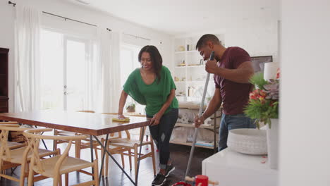 feliz pareja afroamericana de mediana edad barriendo y limpiando la mesa en su comedor, longitud completa