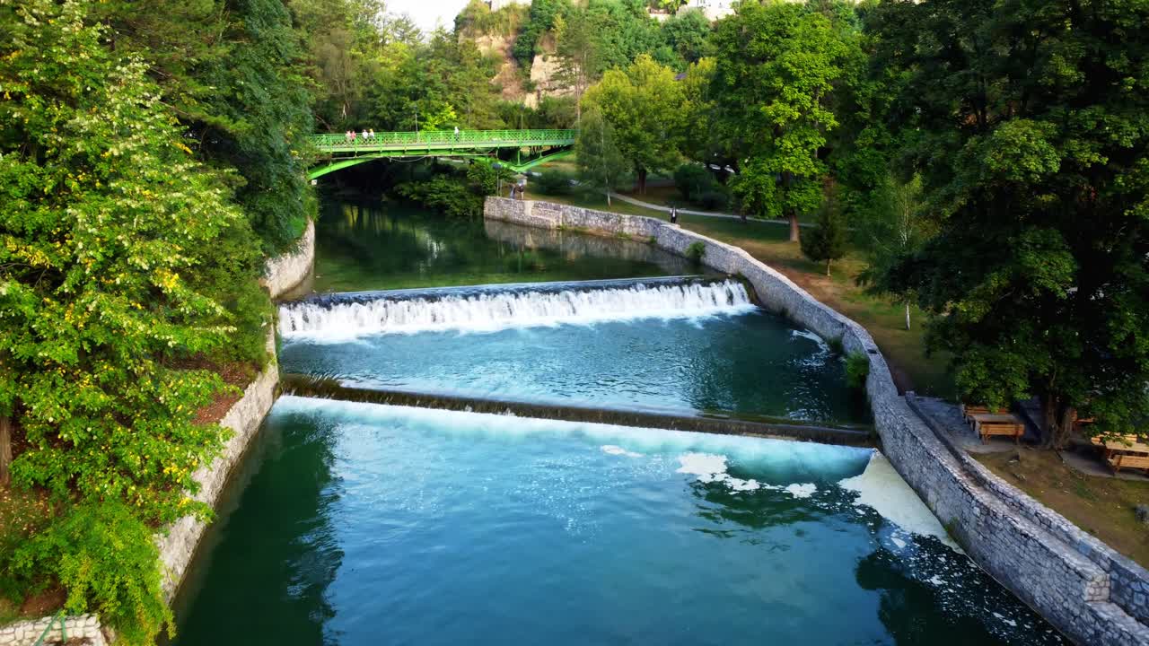 Filmato aereo del fiume Pliva vicino alla cascata di Jajce all'alba in Bosnia ed Erzegovina. Vista aerea del fiume che scorre circondato dal verde, nebbia mattutina e luce calda, ideale per viaggi e professionisti della natura