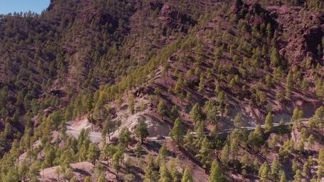 Luftdrohne-Senkt-Sich-In-Felsige-Waldbergstraße-Mit-Geparktem-Auto-Und-Anderen-Vorbeifahrenden-Autos-In-Hohen-Bergen-Auf-Gran-Canaria,-Spanien