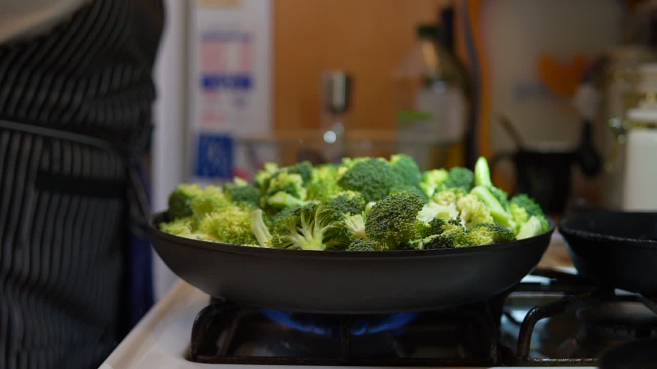 Sprinkling salt on a skillet full of broccoli as it cooks on the stove top - slow motion
