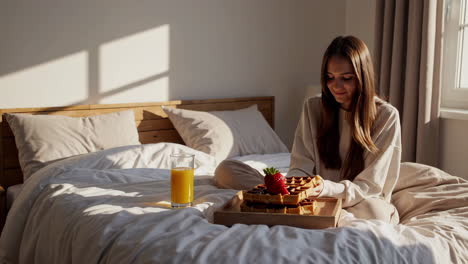 woman eating breakfast waffles in bed
