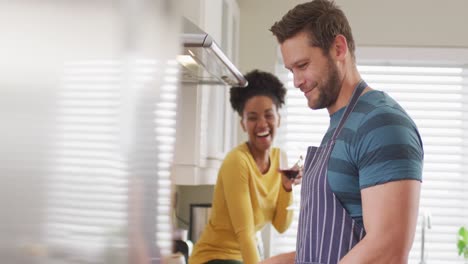 Video-De-Una-Pareja-Feliz-Y-Diversa-Preparando-Comida,-Bebiendo-Vino-Y-Divirtiéndose-En-La-Cocina