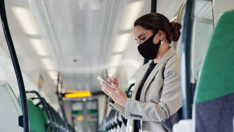 businesswoman stands in train carriage using mobile phone wearing ppe face masks during pandemic