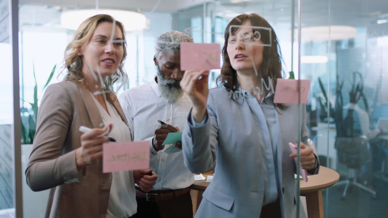 uomini d'affari che usano note adesive brainstorming team leader donna che lavora con i colleghi scrivendo su lavagna di vetro che mostra la strategia di risoluzione dei problemi in riunione in ufficio