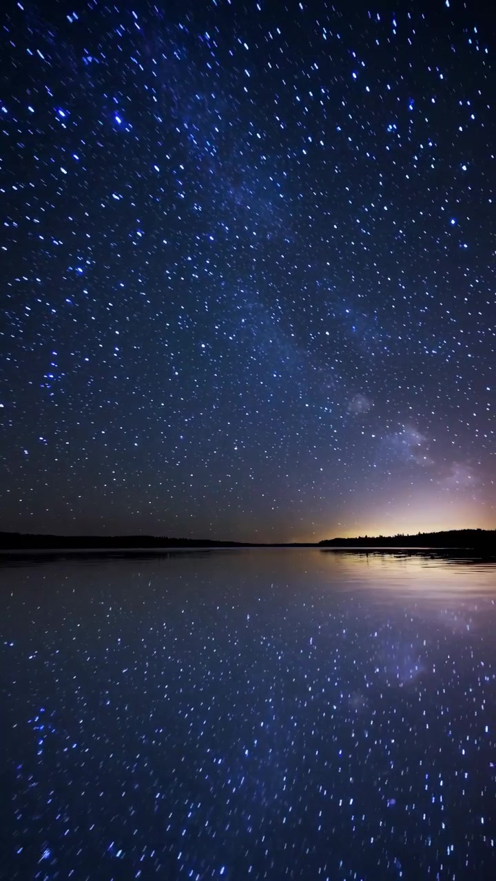 Time lapse del cielo notturno stellato riflesso in un lago calmo.