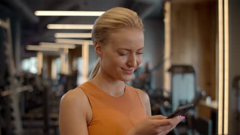 romantic sportswoman texting message in sport club. athlete girl standing at gym