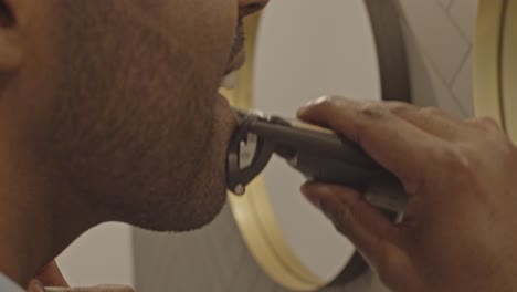 man in bathroom shaving his mustache and beard with a electronic trimmer