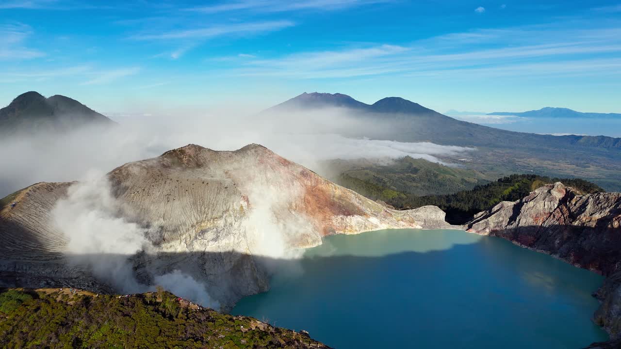 Drone establishing dolly of Ijen crater lake and sulfur clouds reveals harsh volcanic terrain, East Java, Indonesia, stunning water and landscape