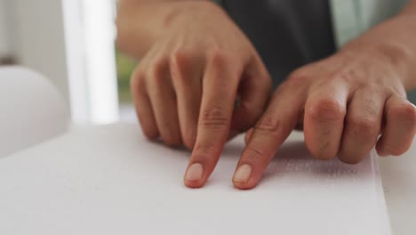 midsection of biracial man sitting at table in kitchen reading braille