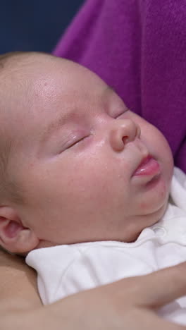 caring mother is holding baby and shaking her child tenderly. baby boy sleeping sweetly in mommy's hands. mom stroking baby cheek with her finger. vertical video