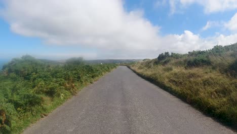 driving car pov on countryside road with sea and grteen moorland and cloudy blue sky north devon uk 4k