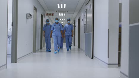 Diverse-female-doctors-wearing-face-masks-walking-in-hospital-corridor