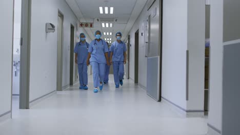 diverse female doctors wearing face masks walking in hospital corridor