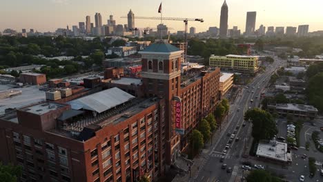 Aerial-of-Ponce-City-Market-building-and-neighborhood-under-sunset-sky,-Atlanta-skyscrapers-in-the-background,-Georgia,-USA