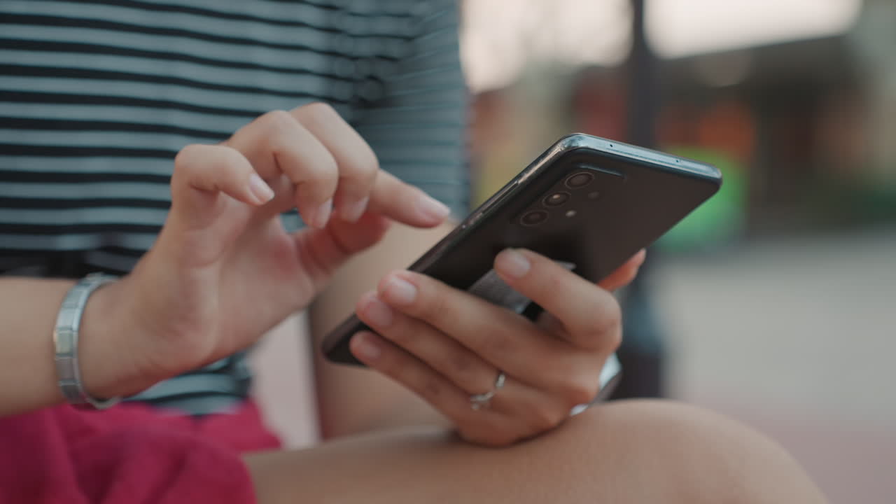 Mani di donna birazziale che digitano al telefono, dettaglio ravvicinato di unghie, anelli e braccialetto, tocchi e scorrimenti precisi, profondità di campo ridotta che crea uno sfondo sfocato, interazione concentrata per messaggistica e app