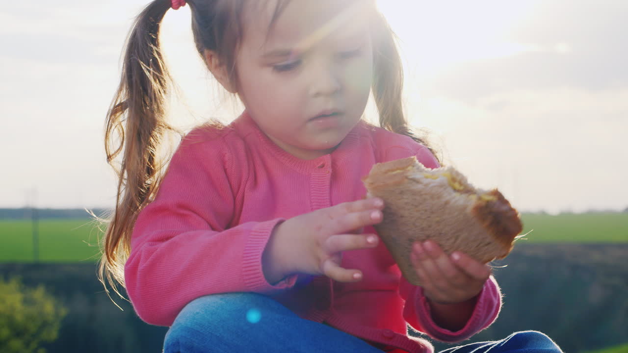 Adorabile bambina che mangia un panino su una radura soleggiata.