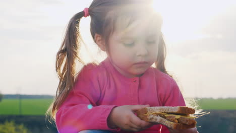 linda niña comiendo un sándwich en un claro soleado