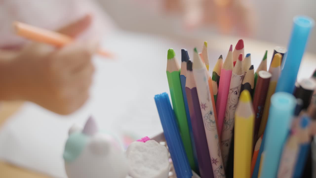 Bir masada oturan, renkli pastel boyalarla çizim yapan küçük kız. Rahat bir iç mekanda yaratıcılık, çocuk gelişimi, öğrenme ve sanat etkinlikleri temaları için idealdir.