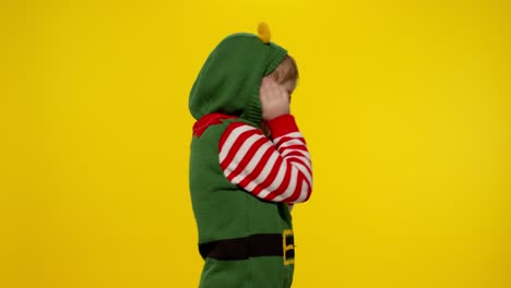 scared kid girl in christmas elf santa helper costume looking aafraid, hiding face with hands