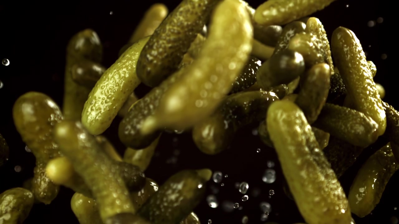 Cornichons tombant au ralenti avec des éclaboussures d'eau sur fond noir