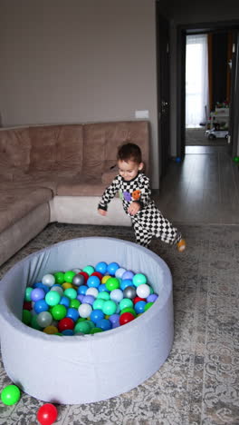baby boy runs up to a dry pool and dives into it. happy kid sits in the basin moving the balls. vertical video.