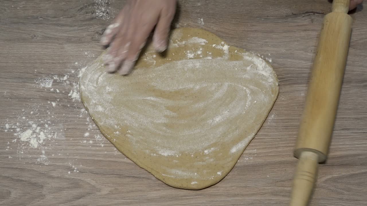una mujer hace pizza en casa. aplana un pedazo de masa amarilla en la mesa de madera con un rodillo. el concepto de cocinar. primer plano. la vista desde arriba. sin rostro. 4k.