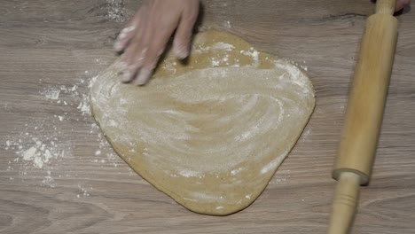 a woman makes pizza at home. she flattens a piece of yellow dough on the wooden table with a rolling pin. the concept of cooking. close-up. the view from the top. faceless. 4k.