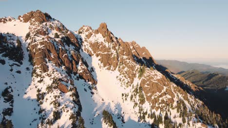 an ascending and looking down drone shot of a snowy peak in the olympic mountains taken from just outside the national park at sunset