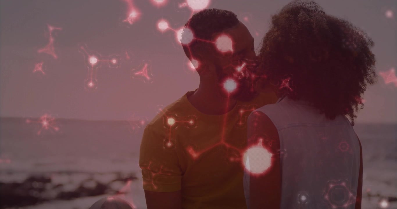Homme barbu étreignant une femme aux cheveux bouclés sur la plage, affichant une superposition de réseau rouge pour la technologie.