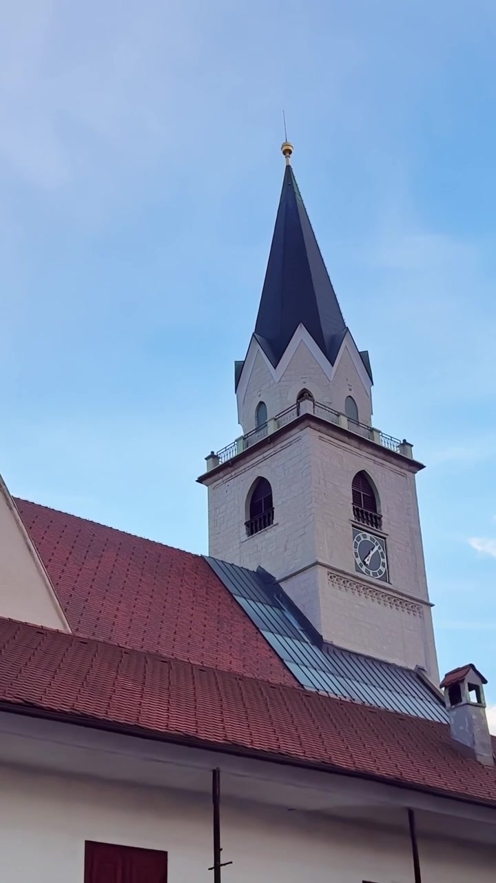 Torre do relógio da Igreja de São Cantiano e telhado de telhas vermelhas na histórica Kranj, Eslovênia, aproximação lenta vertical