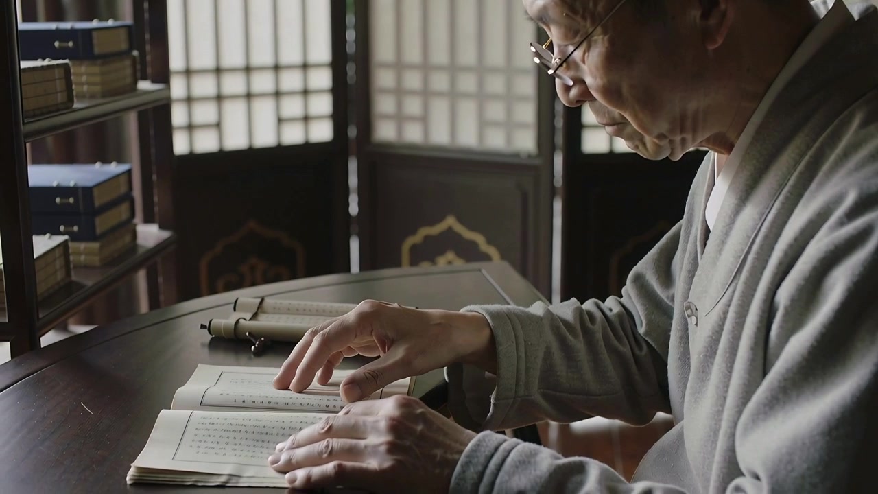 Adjusting thin glasses, scholar in gray robe leaning at study table, tracing book pages, studying