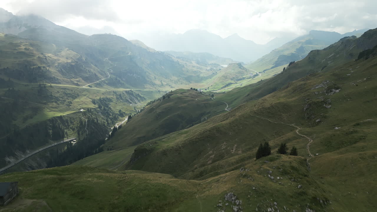 Drone aerial view from the mountain into the sunlit valley in the Bregenz Forest in Austria. In the far background are sun steels and cloud layers.
