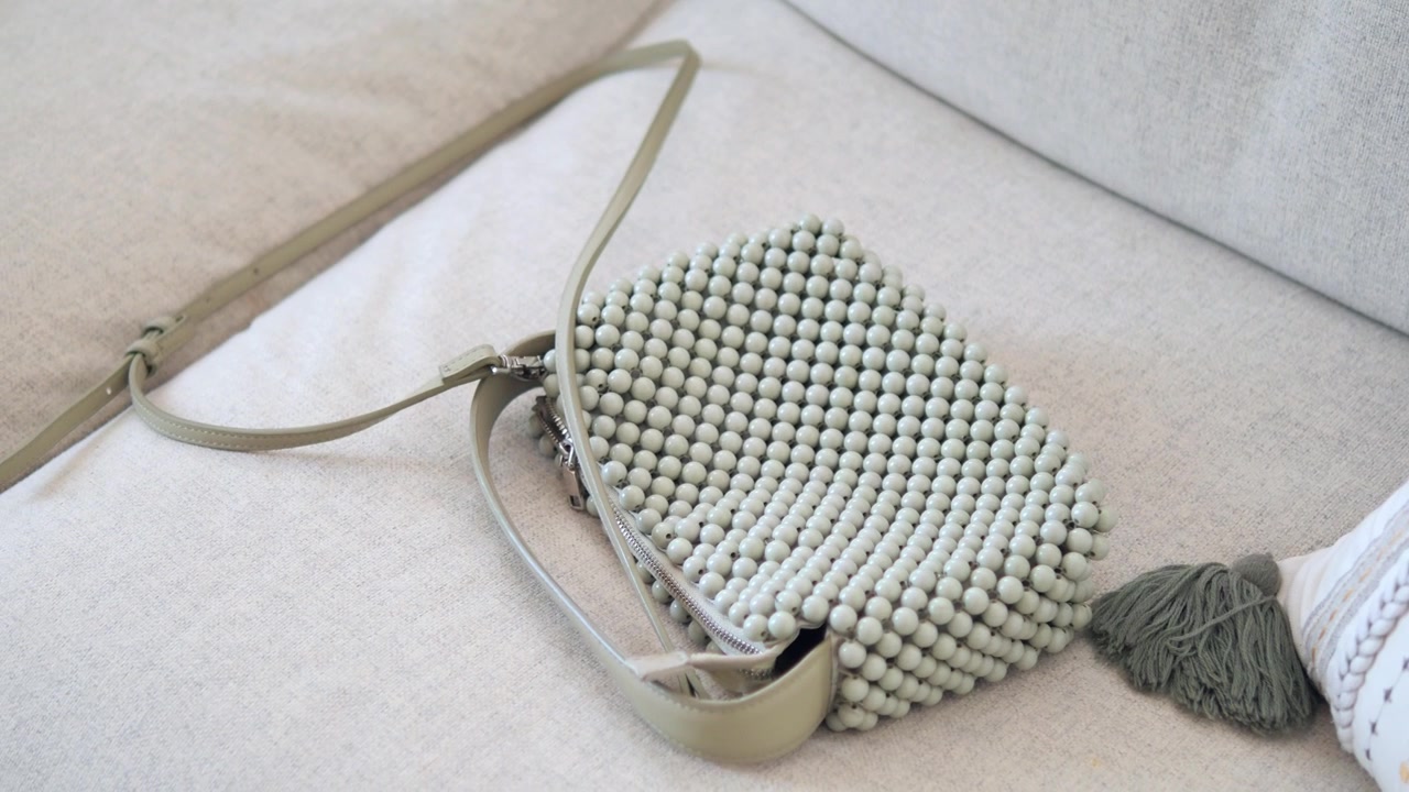 Borsa a tracolla verde salvia con perline appoggiata su un divano