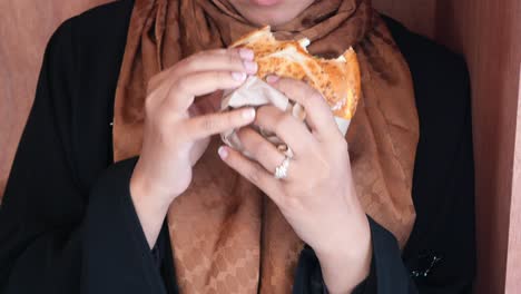 a woman in a hijab eats a sandwich