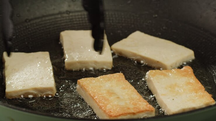 gebratener tofu mit sesamkerne und gewürzen auf einer gusseisenpfanne, zum kochen von japanischem salat. gesunder bestandteil zum kochen veganer vegetarischer diätnahrung. gerösteter tofu über schwarzem hintergrund.