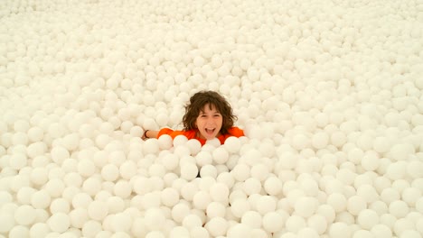 a cute 9-10 years old girl having fun among lots of white ball in a ball pit. 4k slow motion